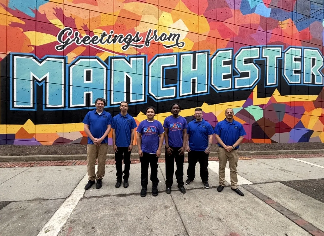 The EAM Moving crew in Manchester, NH in front of the Greetings from Manchester mural
